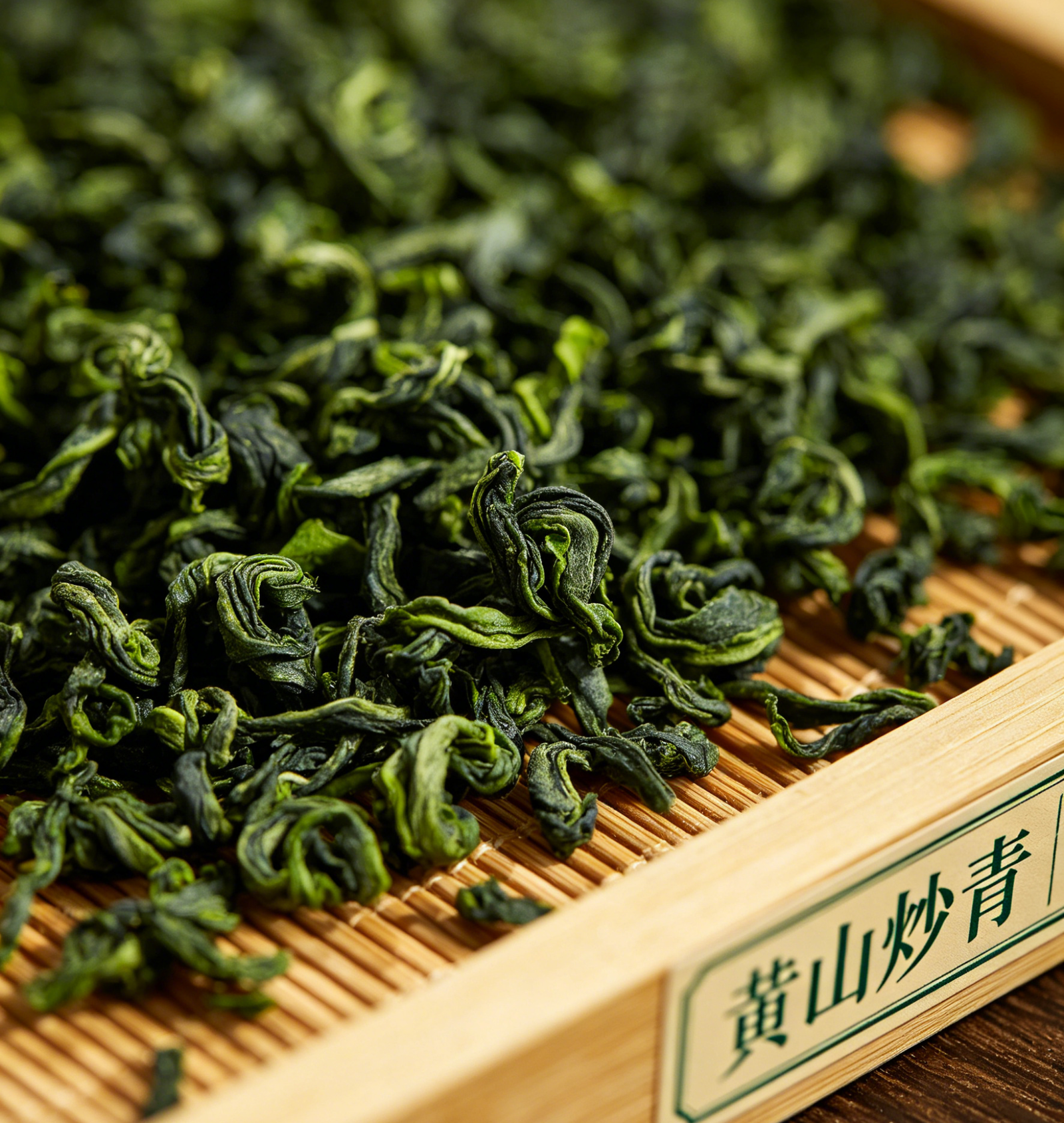 Dry Huangshan Chaoqing green tea leaves, tightly twisted and deep green, piled on a bamboo tray with a Chinese label reading Huangshan Chaoqing