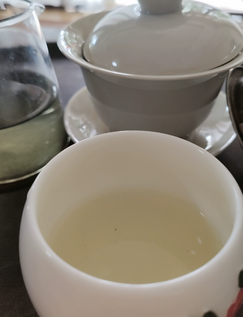 Pale yellow-green Chaoqing liquor in a white cup beside a white gaiwan and a glass fair pitcher