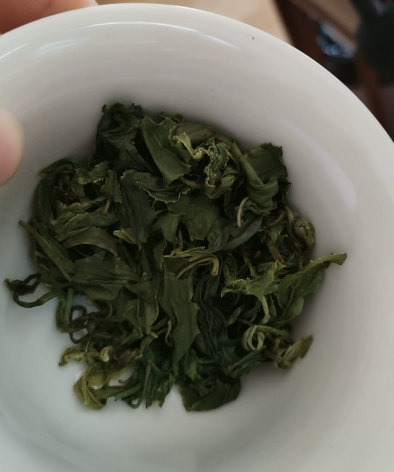 Wet, unfurled Huangshan Chaoqing green tea leaves at the bottom of a white ceramic bowl, twisted everyday leaf rather than a showpiece shape