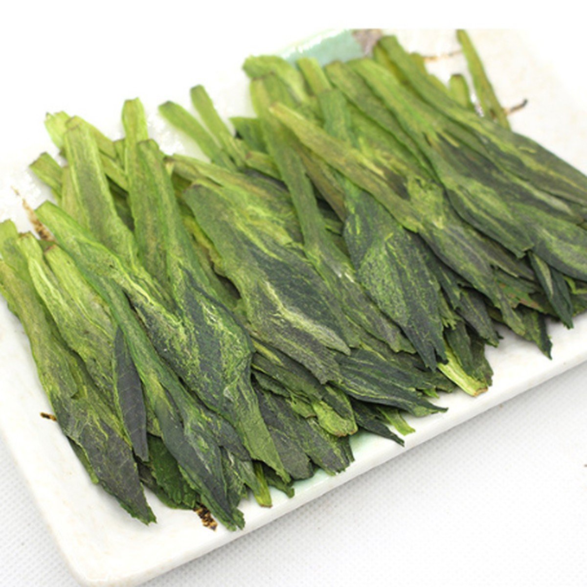Long, flat Taiping Houkui leaves laid on a white plate, each a set of two leaves pressed around a bud