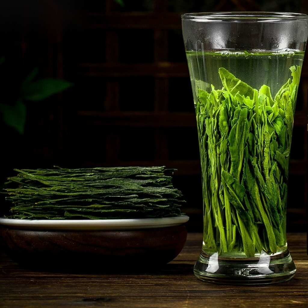 Dry Taiping Houkui beside a tall glass with standing leaves