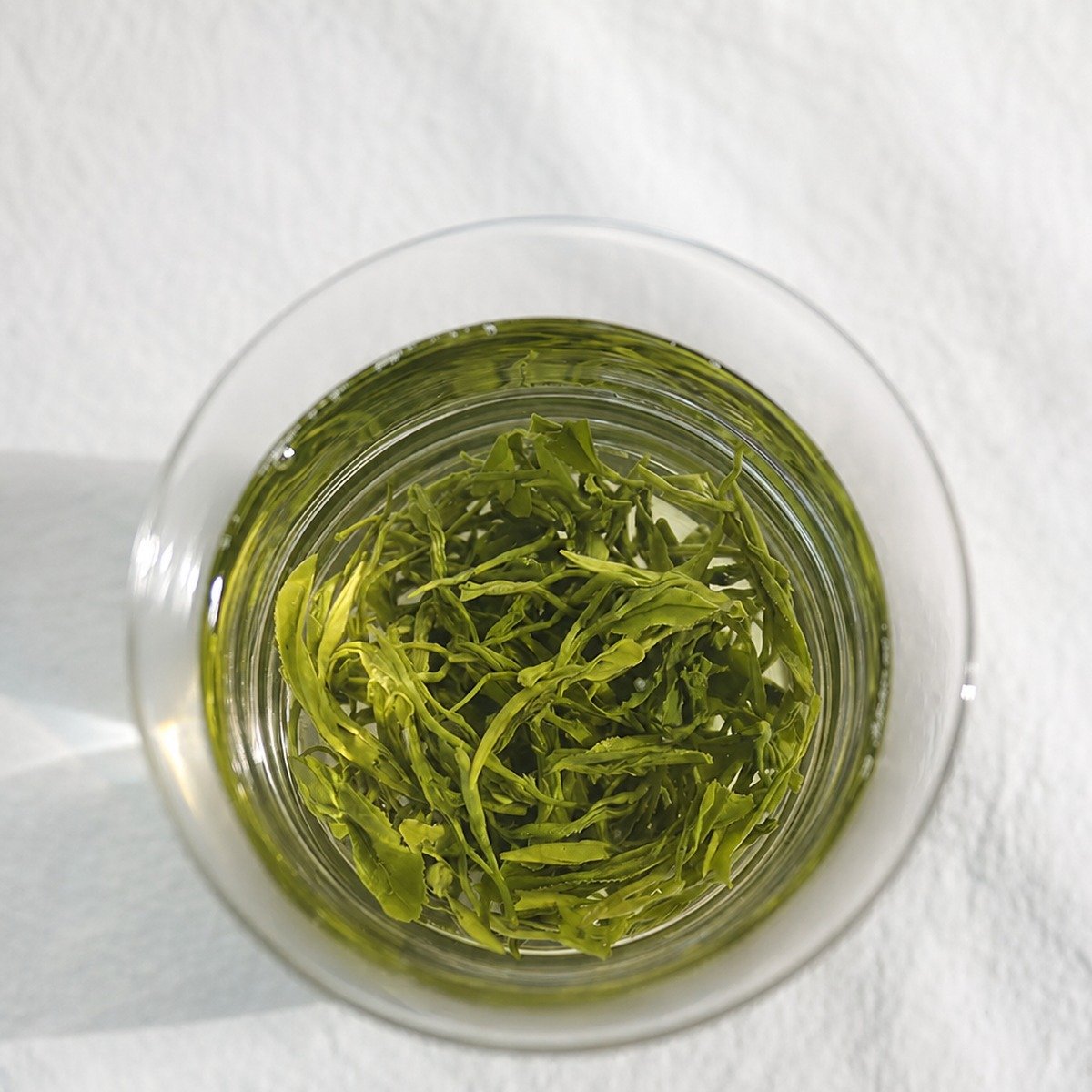 Top-down view of a clear glass of Huangshan Maofeng with unfurled green leaves and pale yellow-green liquor