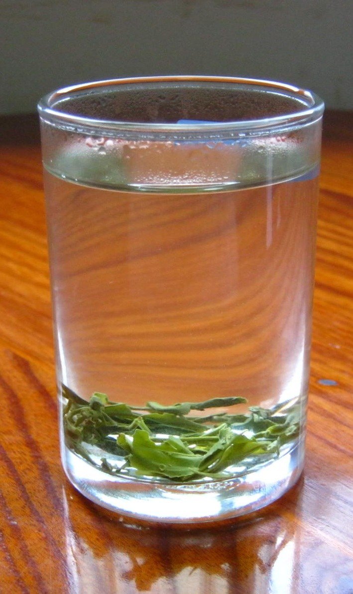 Huangshan Maofeng leaves settled at the bottom of a clear glass of pale tea on a wooden table