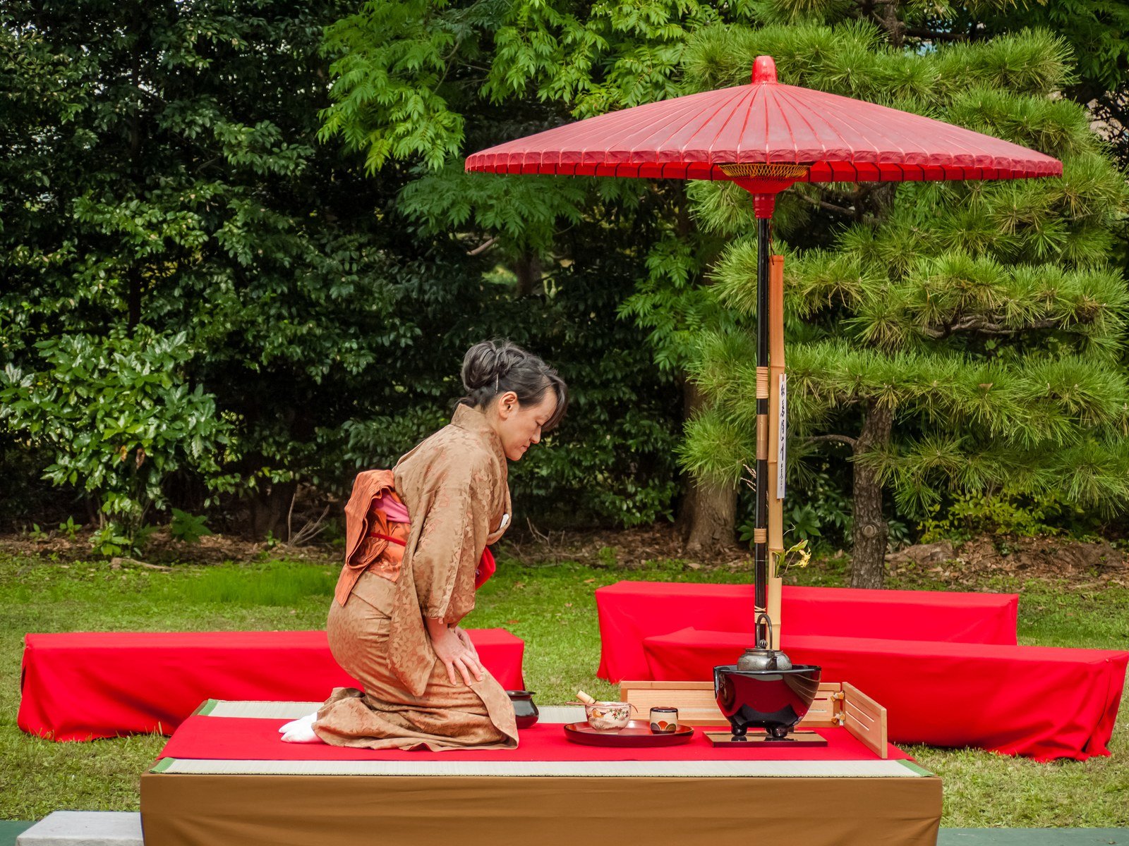 A woman in a kimono kneeling and whisking bright green matcha in a tea bowl during a Japanese tea ceremony